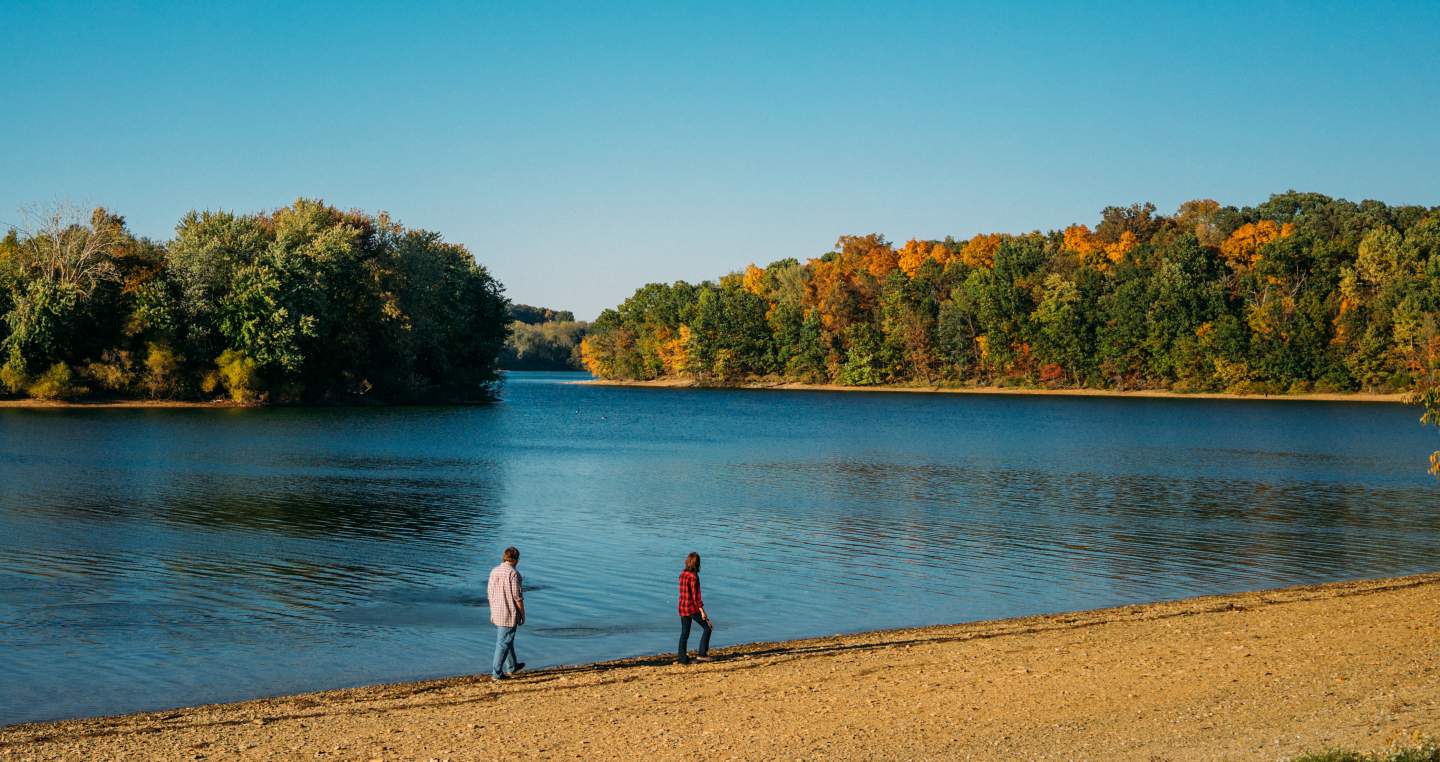 Image of two people strolling along the lake shore in fall under a bright blue sky