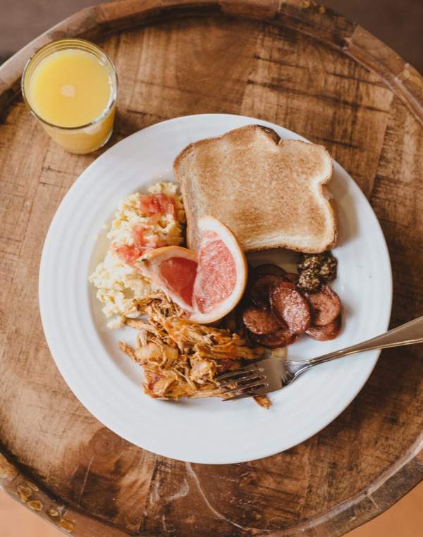 A glass of orange juice sits next to a plate of eggs, toast, grapefruit, and sausage.