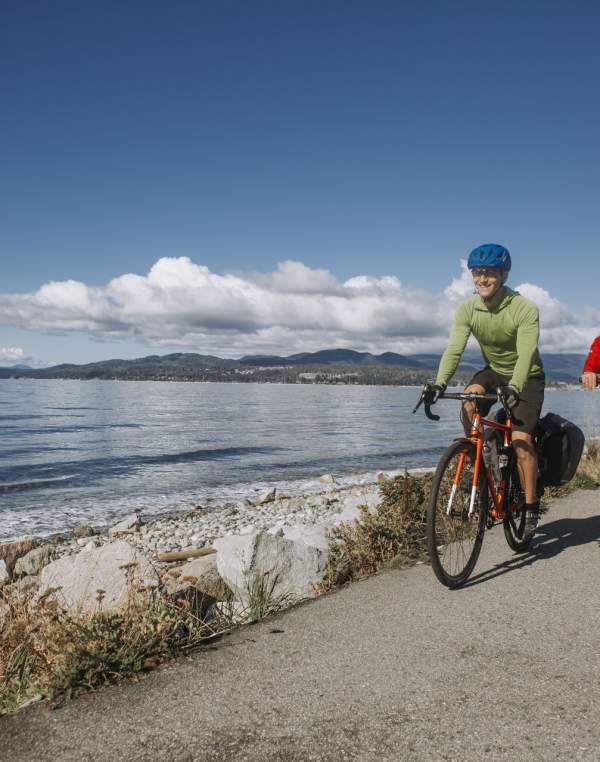 Two cyclists pedal along a trail next to the beach.