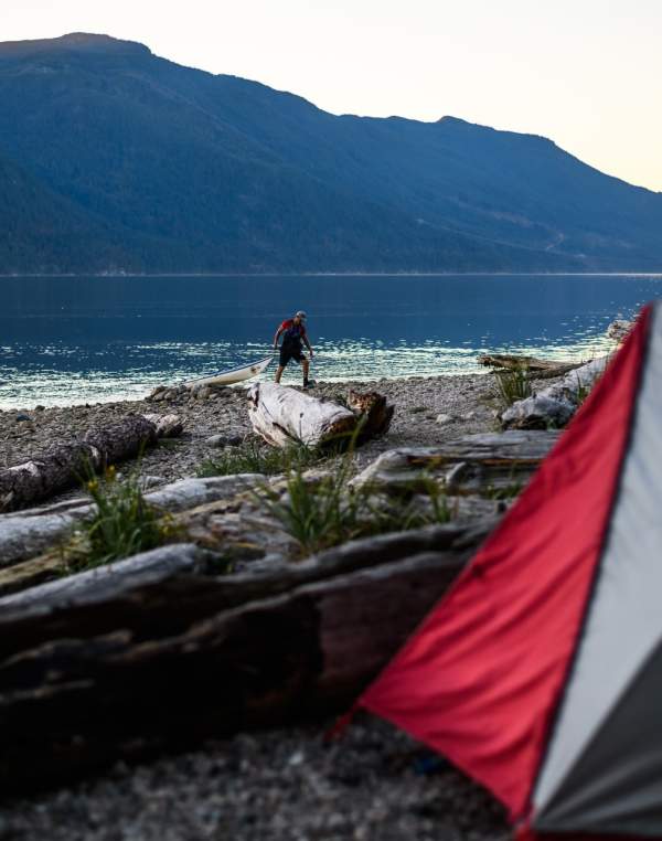 Two people bring their kayaks ashore near their campsite.