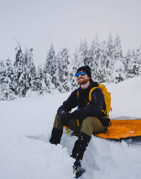 A man grins as he sits down to take a rest from snowshoeing.