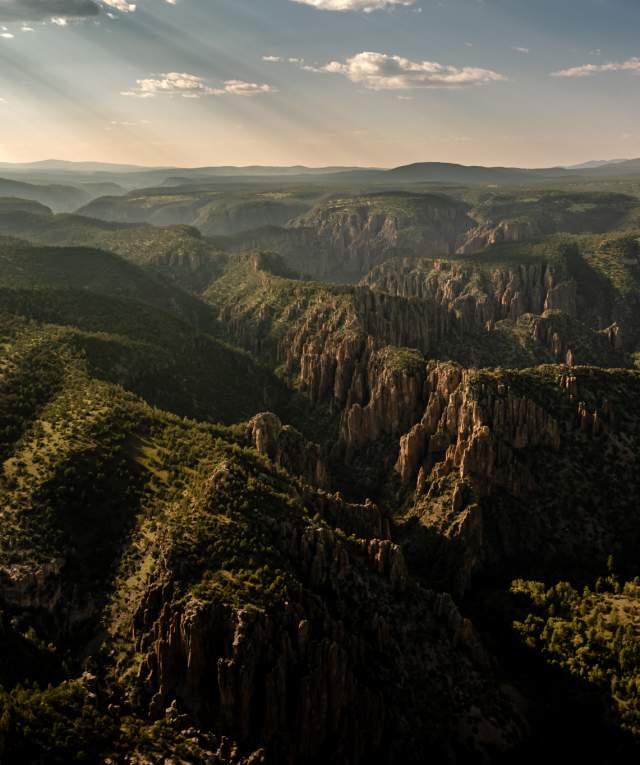 Aerial view of the Gila Wilderness at sunrise, showcasing the vast, rugged terrain and deep gorges under a glowing sky.