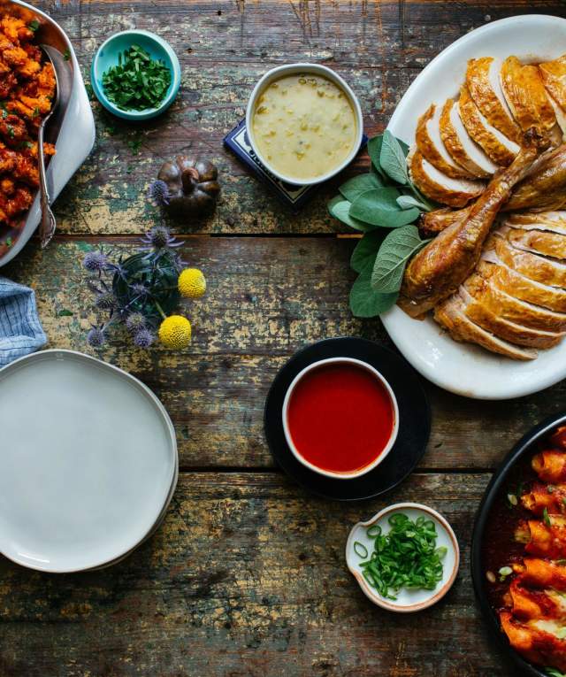 Assorted dishes including roasted turkey and sausages, baked vegetables, and sauces on a rustic wooden table.