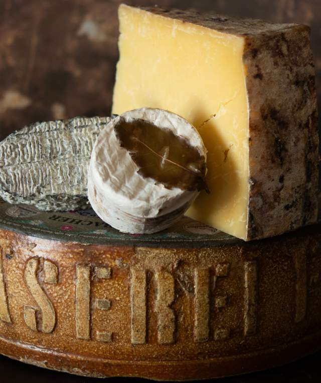 Assorted cheeses, including a wedge of hard cheese and a small round soft cheese, displayed on a rustic wooden cheese board with the inscription "Käserei.