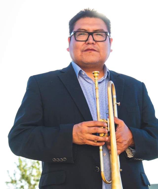 a man in a suit and thick rimmed glasses holds a brass instrument