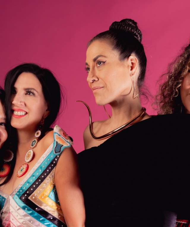 four women in fashionable outfits pose in front of a pink backdrop