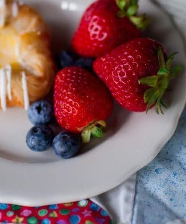 book next to plate of pastry and fruit on bed
