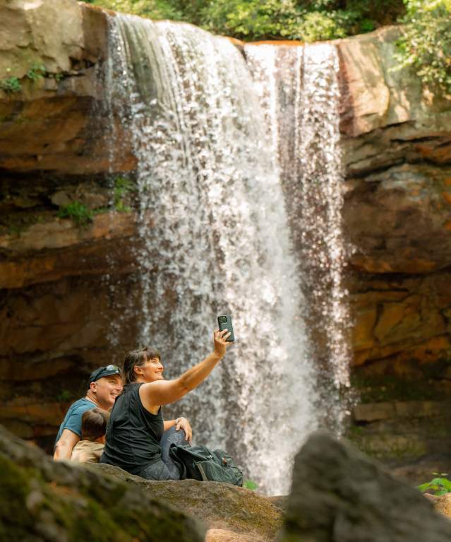 A family takes a selfie in front of a waterfall.