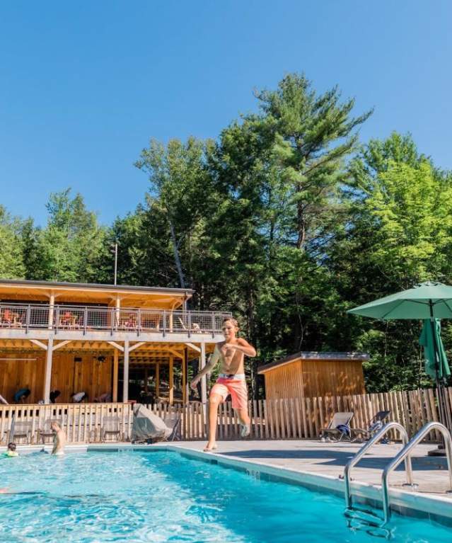 Huttopia Adirondacks swimming pool with person jumping into the water and hotel balcony in background