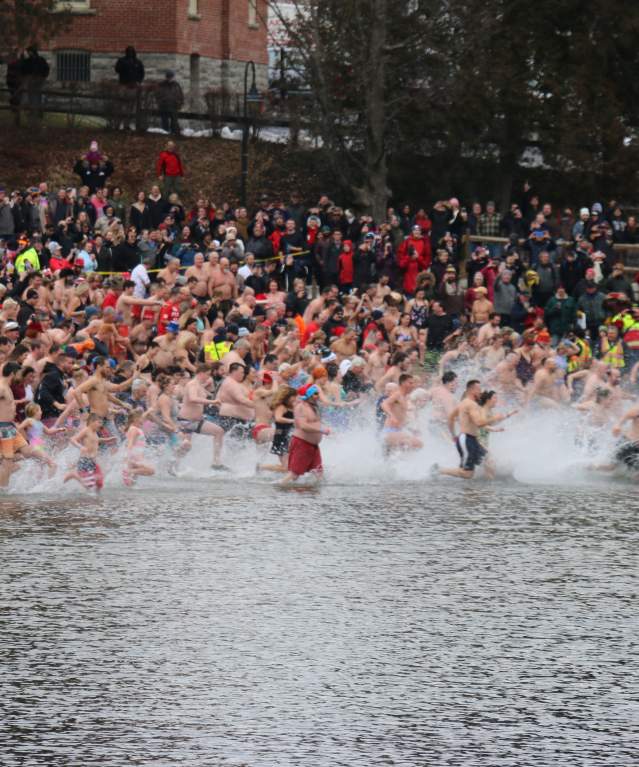 A crowd of swimmers running toward Lake George in winter for the polar plunge event.