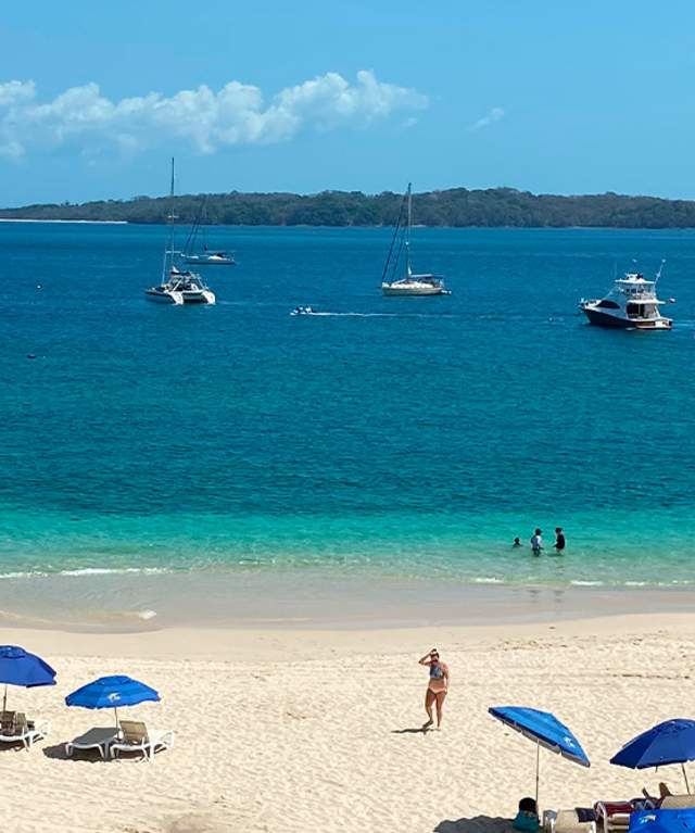Tourists sunbathe. Blue umbrellas scattered on the beach, Boats on the water. Sunny day.