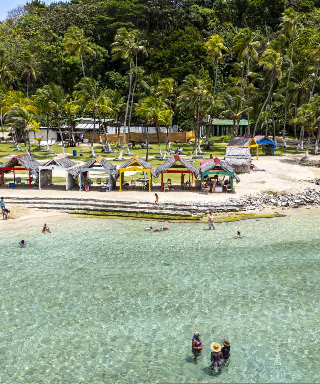 Tourists enjoying a crystal-clear water beach with palm trees in Portobelo, Panama