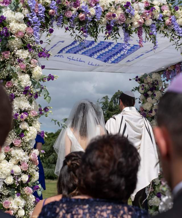 Pareja judía en una ceremonia matrimonial bajo un dosel nupcial de chuppa floral.