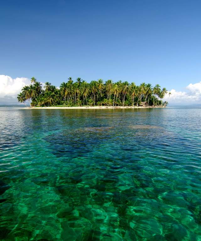 Small island covered in dense vegetation, with a few sandy beaches visible. The water is shallow and clear, with a visible sandy bottom.