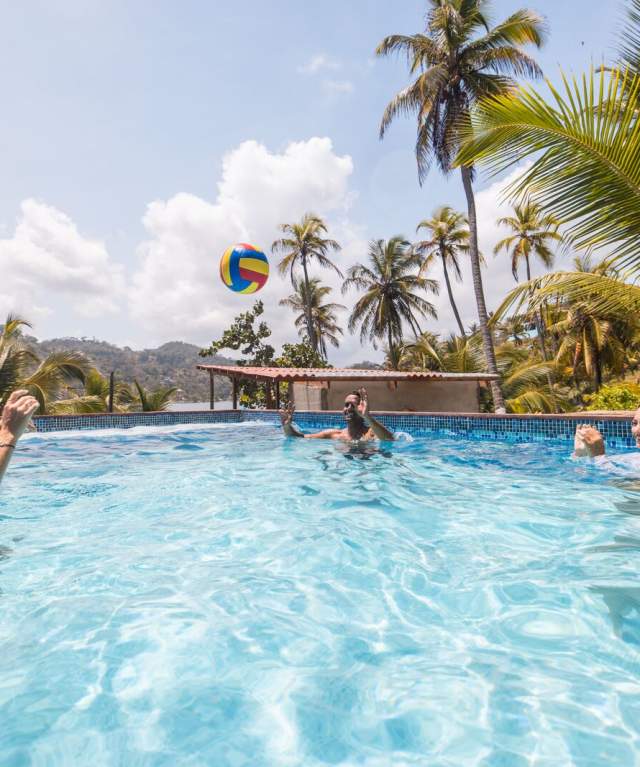 Tourists playing volleyball in a hotel swimming pool surrounded by palm trees in Portobelo, Panama.