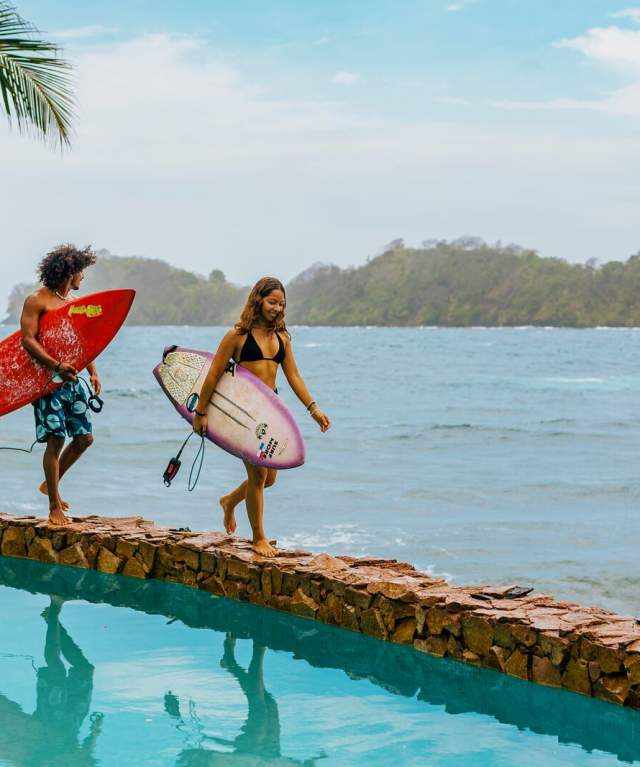 Couple walking near a pool with surfboards, Isla Grande beach can be seen in the background