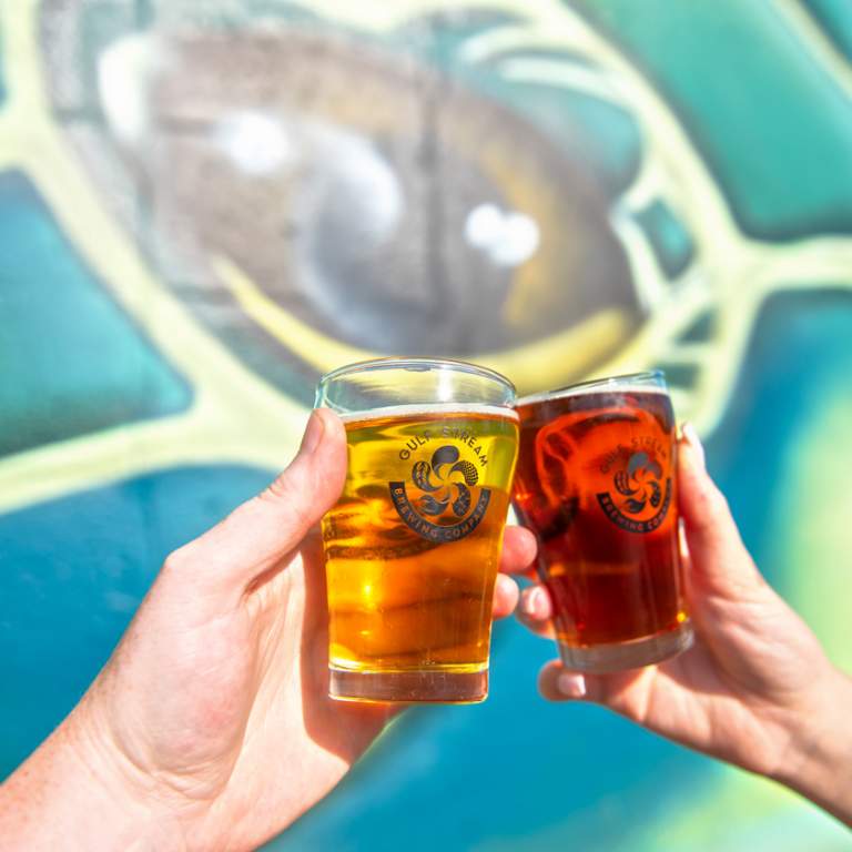 Close-up of two pints clinking in front of a mural at Gulf Stream Brewery in Fort Lauderdale, FL.