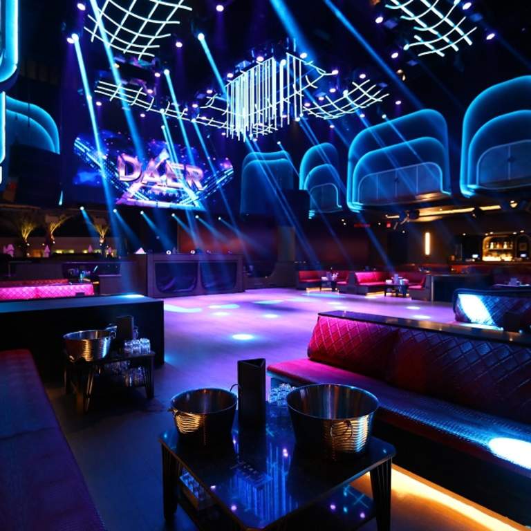 Dark nightclub with purple and blue lights shining all around the room.