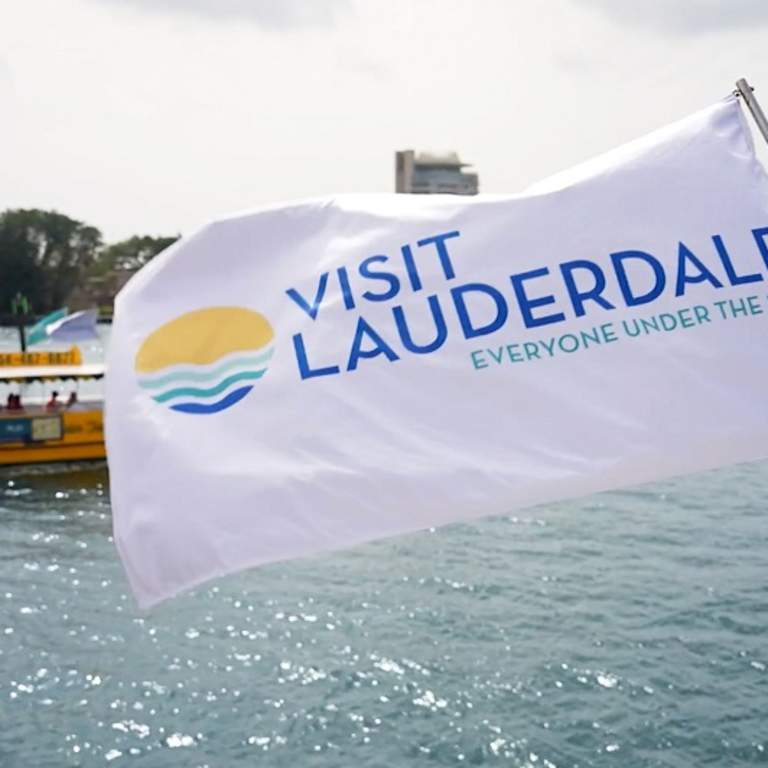 Visit Lauderdale Flag blowing in the wind with the Water Taxi riding behind it.