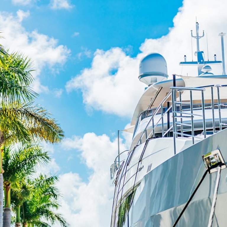 Looking up at a Super Yacht next to palm trees with a blue sky with puffy white clouds