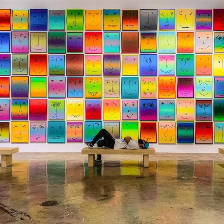 A man laying on a bench in front of the Happy Exhibit at NSU Art Museum