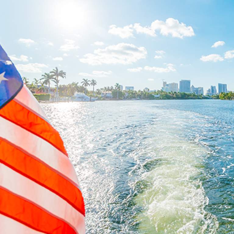 An American flag blowing in the wind on the back of a boat in the water