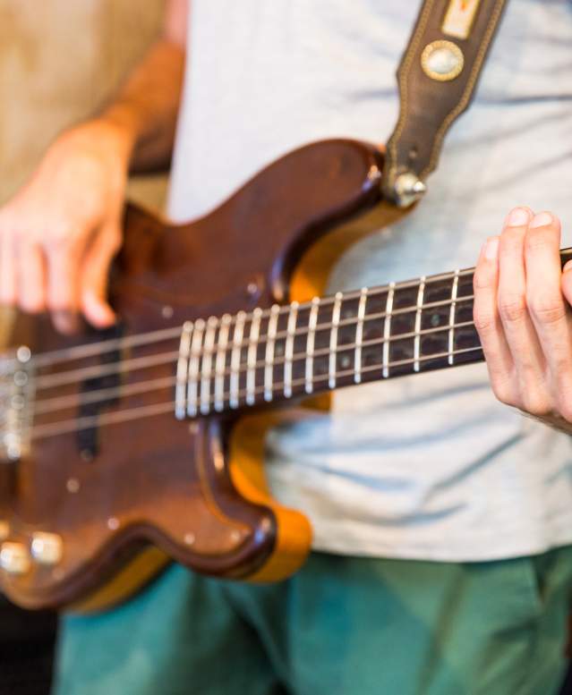 A close up of a guy strumming a brown guitar.