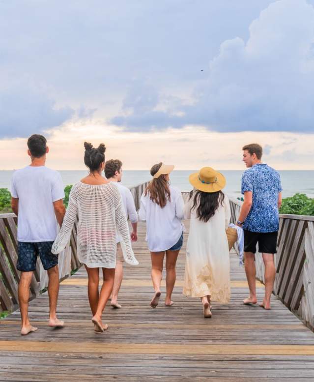 Six friends walking down a baordwalk to the beach.