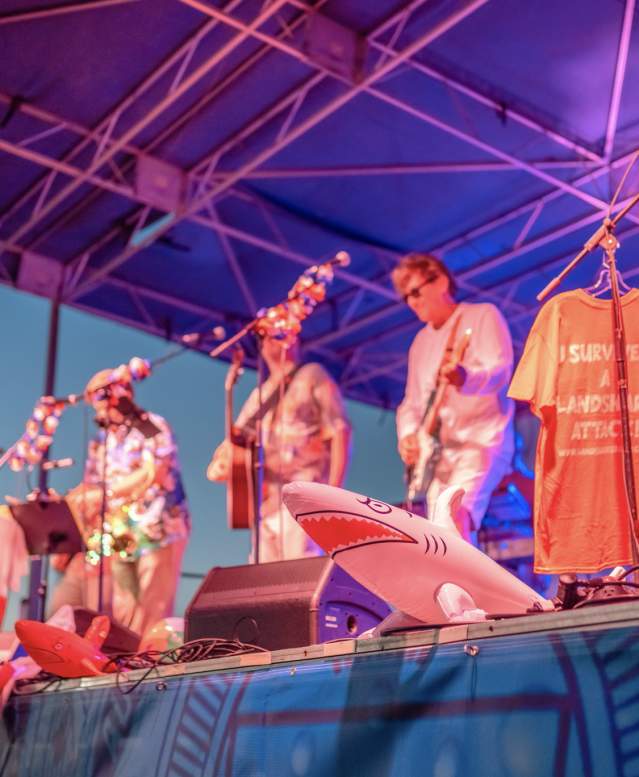 A band performs on a brightly-lit stage decorated with leis and inflatable sharks
