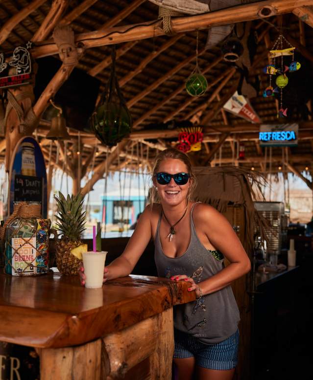 A bartender passes a drink over a wooden tiki bar