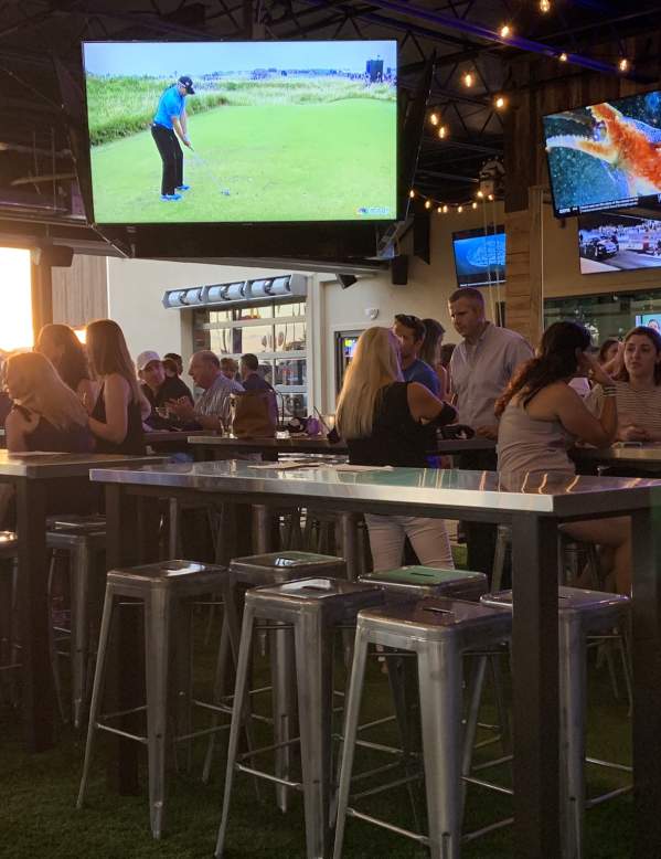 Big screen TV and patrons sitting at high table tops at Little Woodrow's Sports Bar
