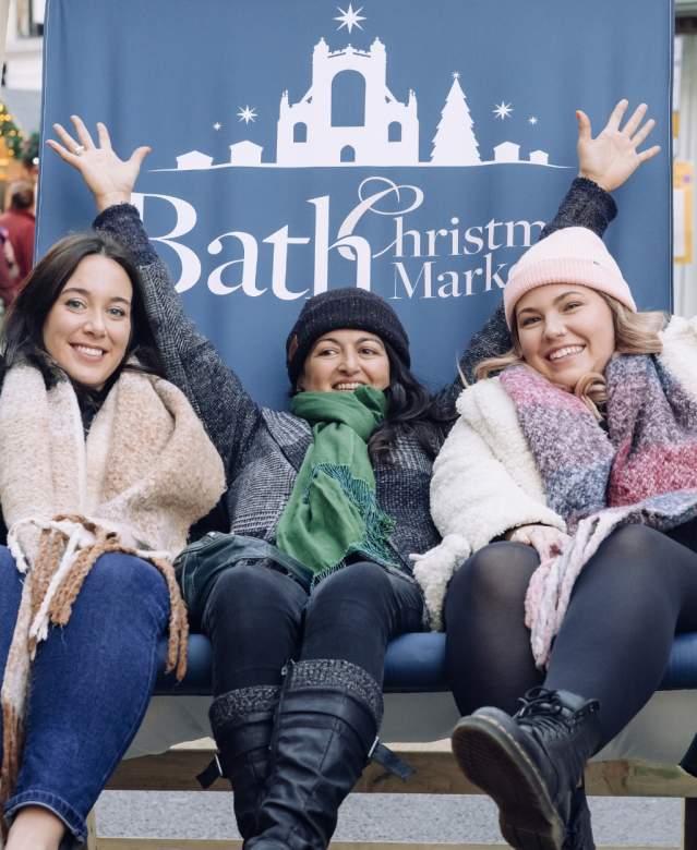 3 women sat in a beach style pop up chair that has Bath Christmas Market written on it