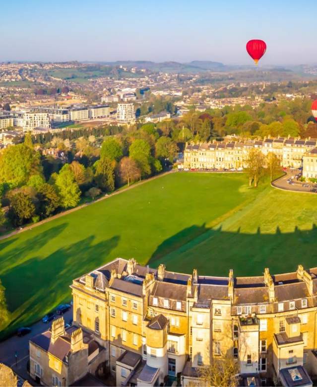 An aerial view of the Royal Crescent in Bath near Bristol, with hot air balloons launching from the green