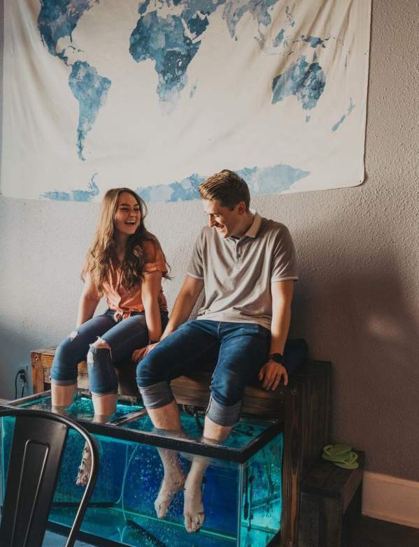 A couple are sitting on a bench with their feet in a FishKiss tank.