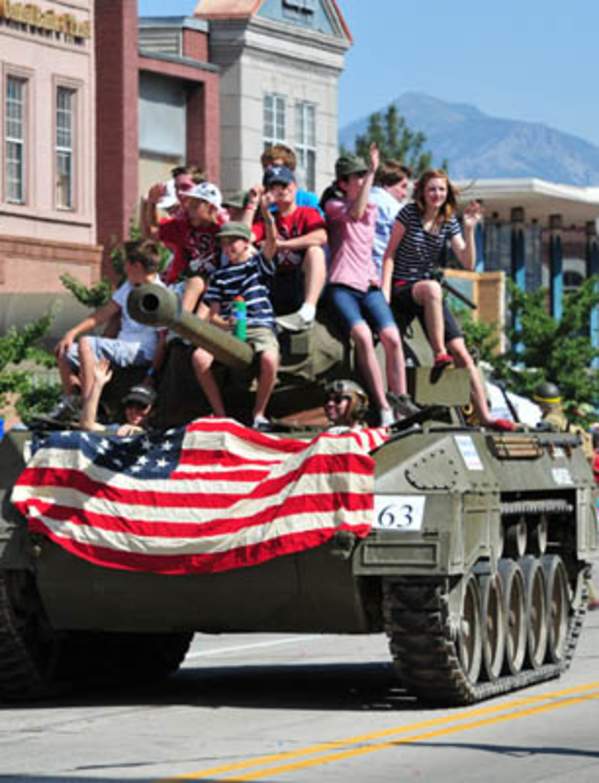 Freedom Festival parade tank going down road with American flag on it and riders on it
