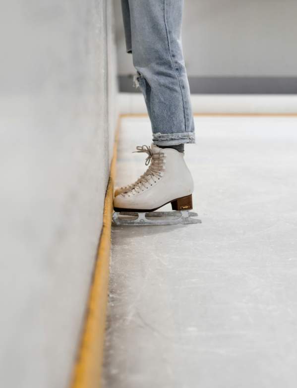 ice skater wearing jeans leans against side of the rink