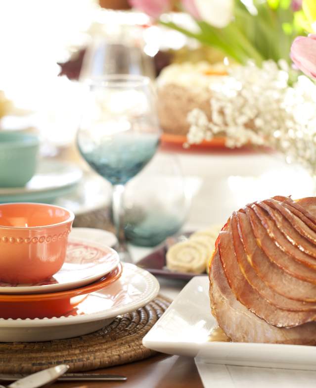Easter Ham Sitting on Table Decorated With Colorful Dish Sets and Tulips