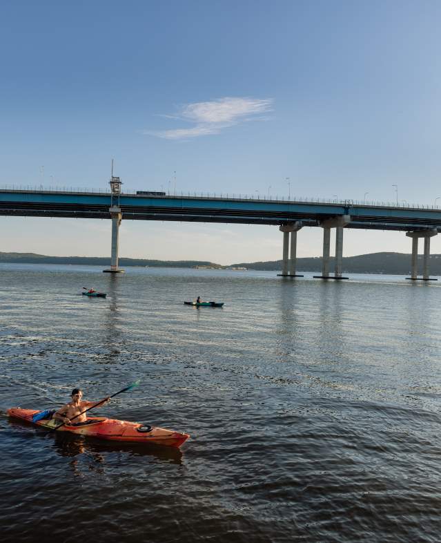 A group of kayakers paddle along the Hudson River at sunset.