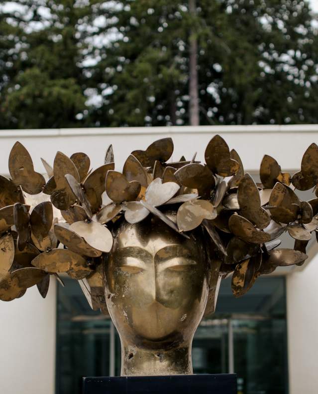 A bronze sculpture of a person's head adorned with a wreath of butterflies on display outside the Katonah Museum of Art.