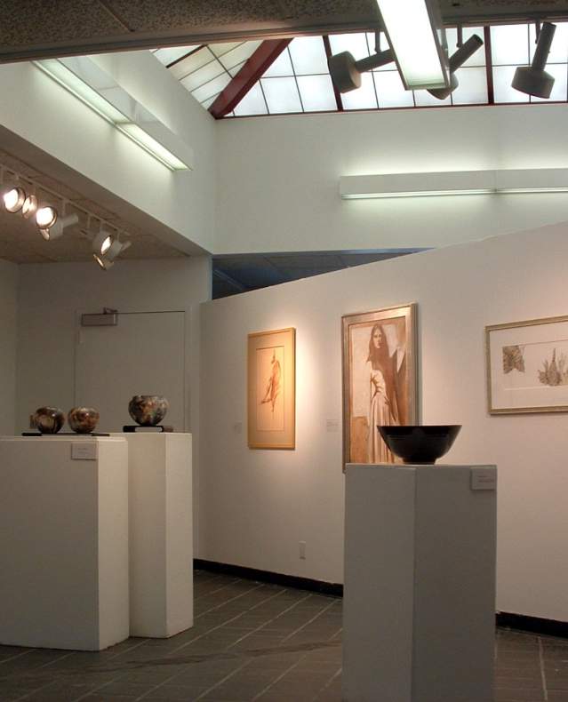 A gallery with pictures hanging on the wall plus displays on stands.