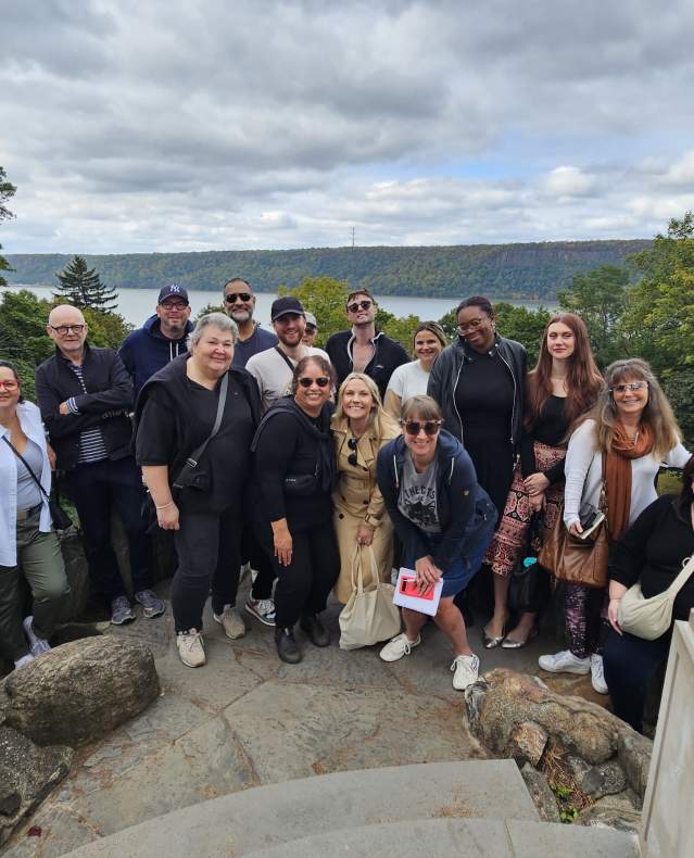A group of travelers poses at Untermyer Gardens with a view of the Hudson River in the background.