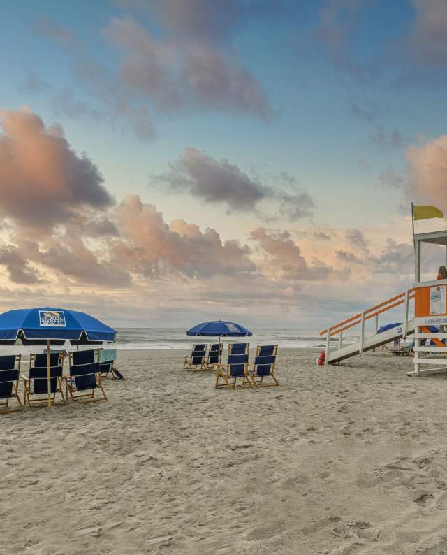 A beautiful sunrise in North Myrtle Beach with beach chairs, umbrellas, and lifeguard stand.