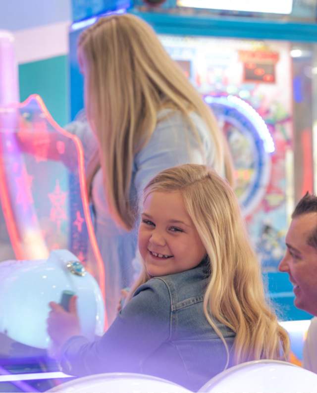 young girl playing an arcade game with her family watching.