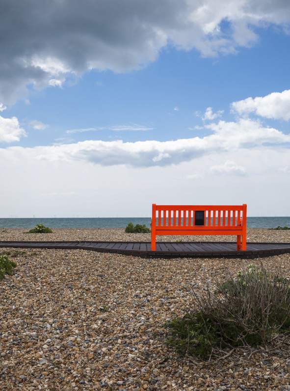 A shingle beach with red bench