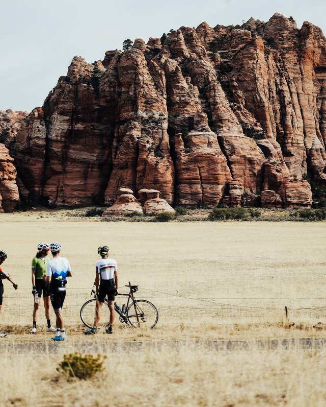 Five cyclists stand in front of a red rock formation in Kanarraville, Utah.