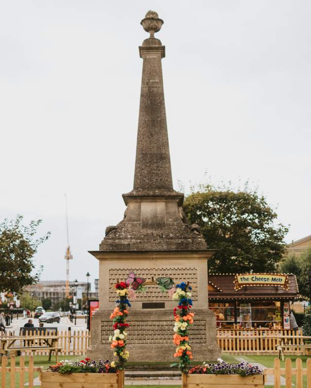 A portrait view of the Obelisk in St Marks Shopping Centre surrounded by flowers and picket fences