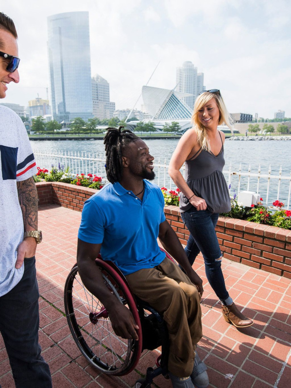 Three friends, including one using a wheelchair, wander along Milwaukee’s lakefront with the skyline in view.