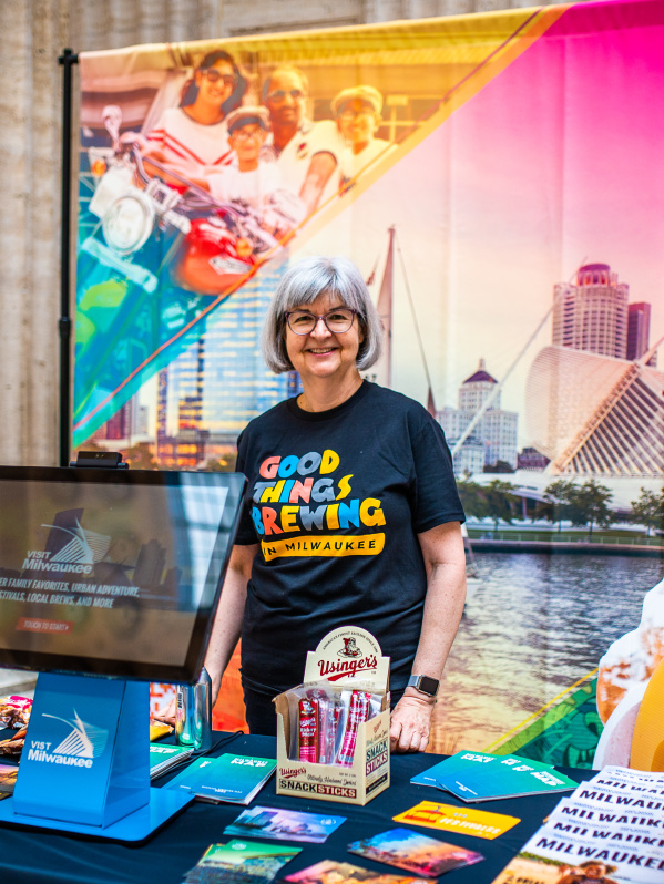 smiling volunteer stands by Visit Milwaukee display at union station