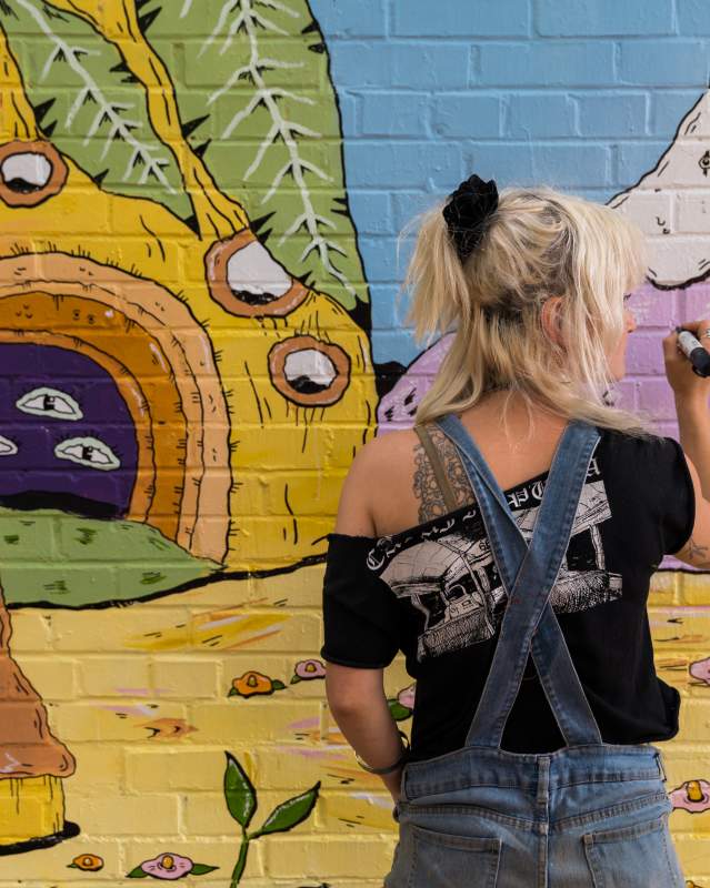 Artist painting a wall mural within the Plaza Walls collection in OKC's Plaza District