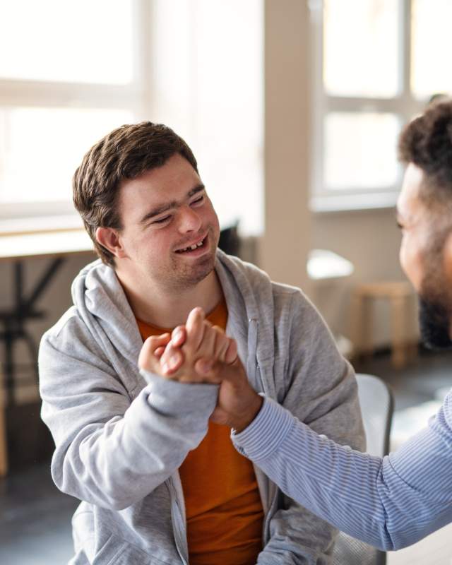 Young happy man with Down syndrome with his mentor celebrating success indoors at school